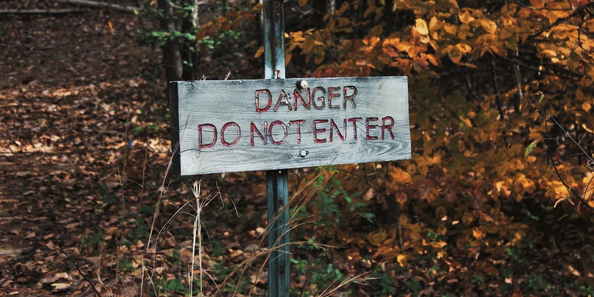 A sign stating "DANGER. DO NOT ENTER" sits in a wooded area