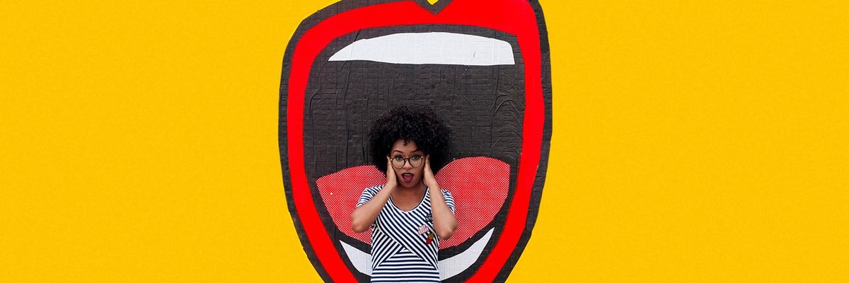 a black woman with glasses covering her ears while standing in front of a mural with a mouth and a yellow background
