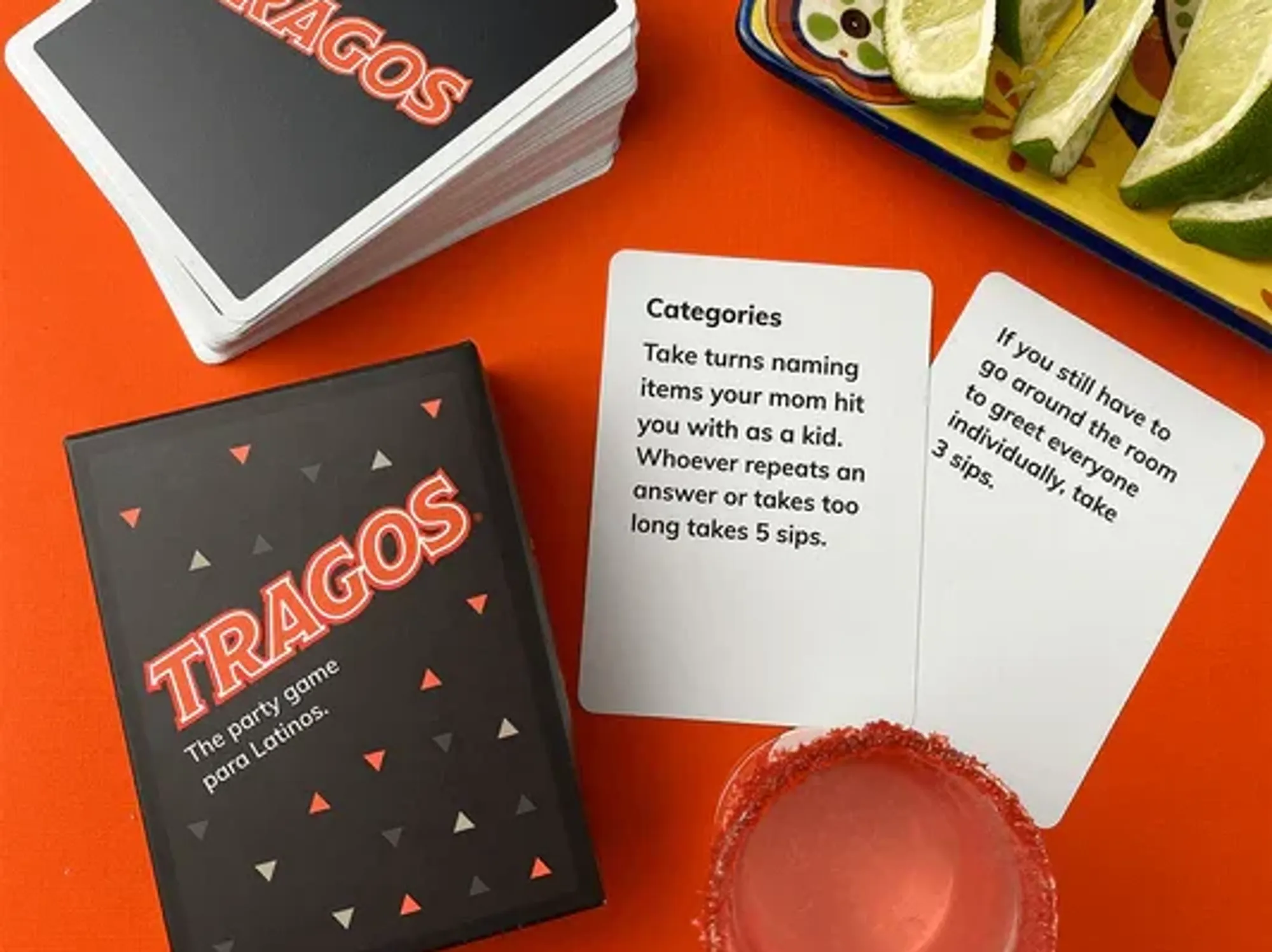 a promotional image for the tragos party game depicting a pair of cards along with a shot and limes