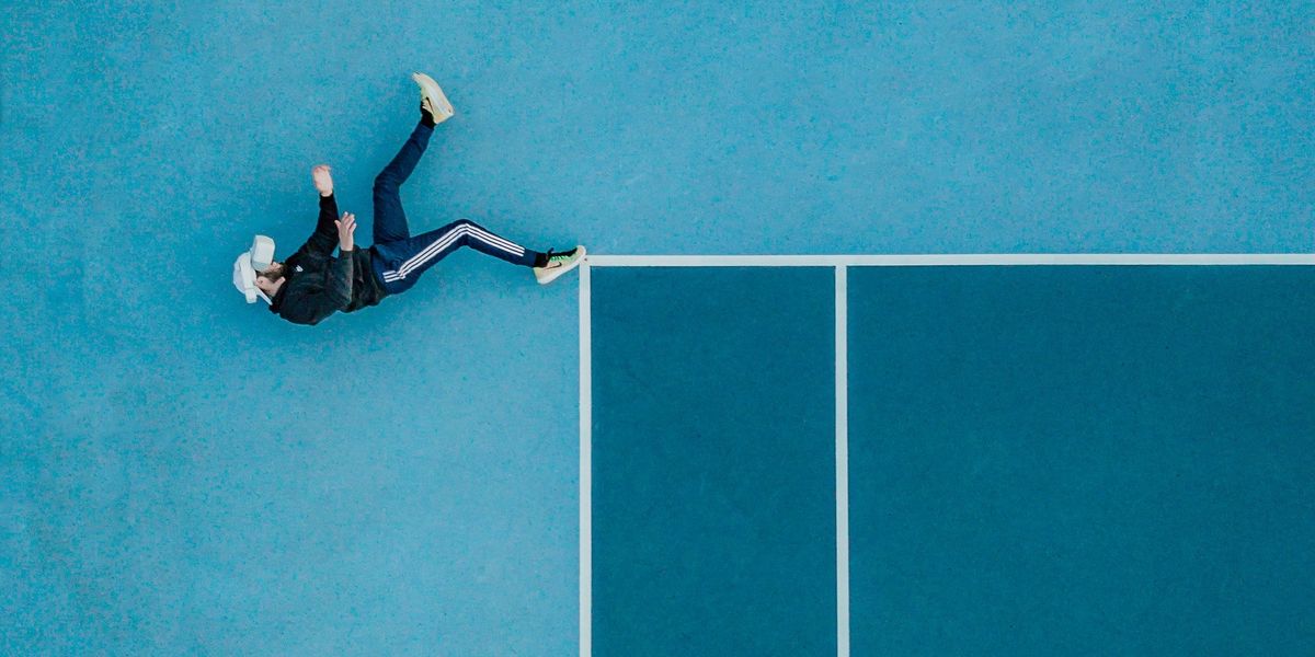 Man lying on edge of tennis court OR man falling off edge of structure