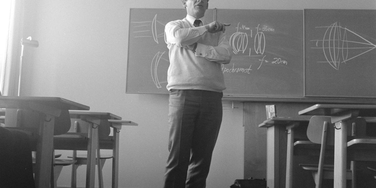 Black and white photo of teacher standing at front of classroom