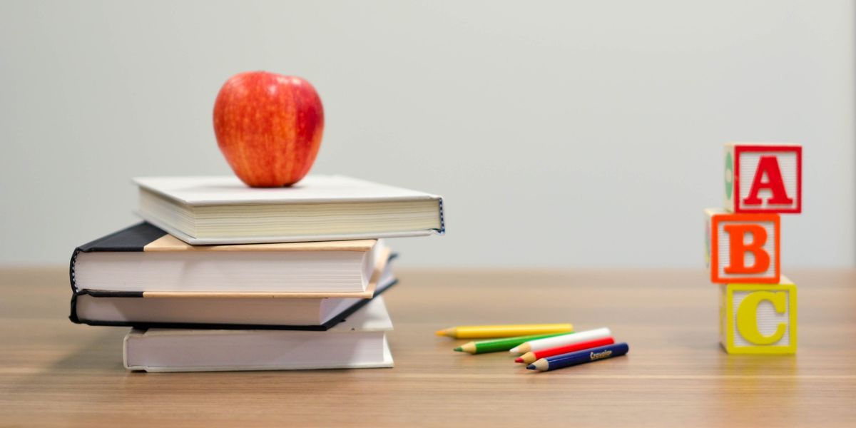 Apple sitting on top of a pile of books, next to colored pencils and ABC blocks.