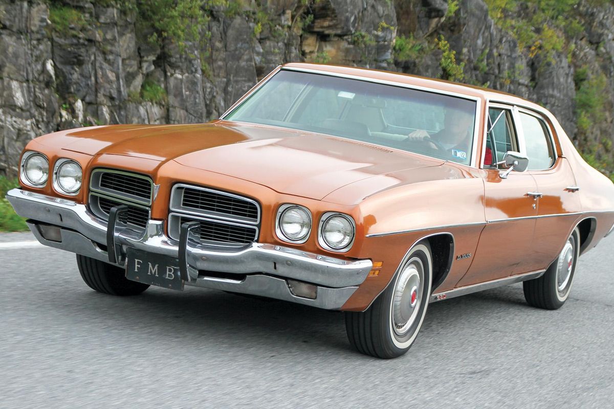 Color image of a 1972 Pontiac Le Mans driving down the road with rocks and mountains in the background, front 3/4 position.