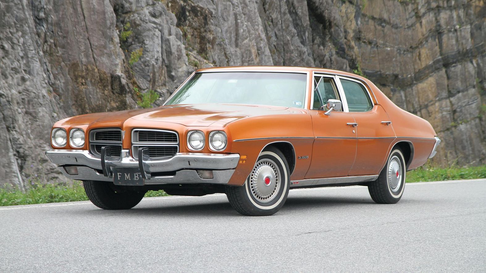 Color image of a 1972 Pontiac Le Mans parked in front of a mountain and rock formation, front 3/4 position.