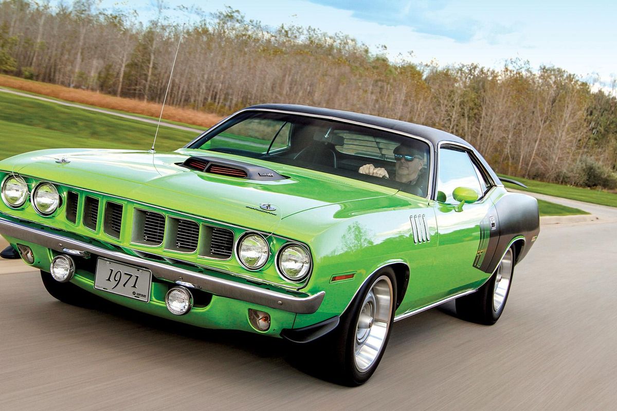 Color image of a modified 1971 Plymouth Barracuda driving down the road in action, front 3/4 position, trees in background.