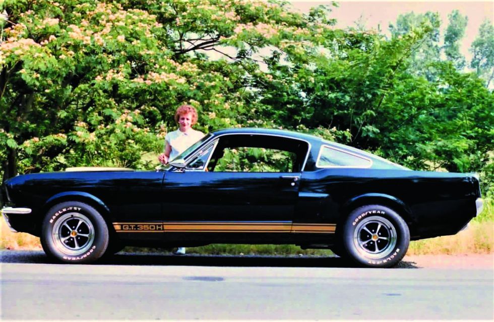Color image of a Shelby G.T. 350 Hertz parked in a profile position with a woman behind it.